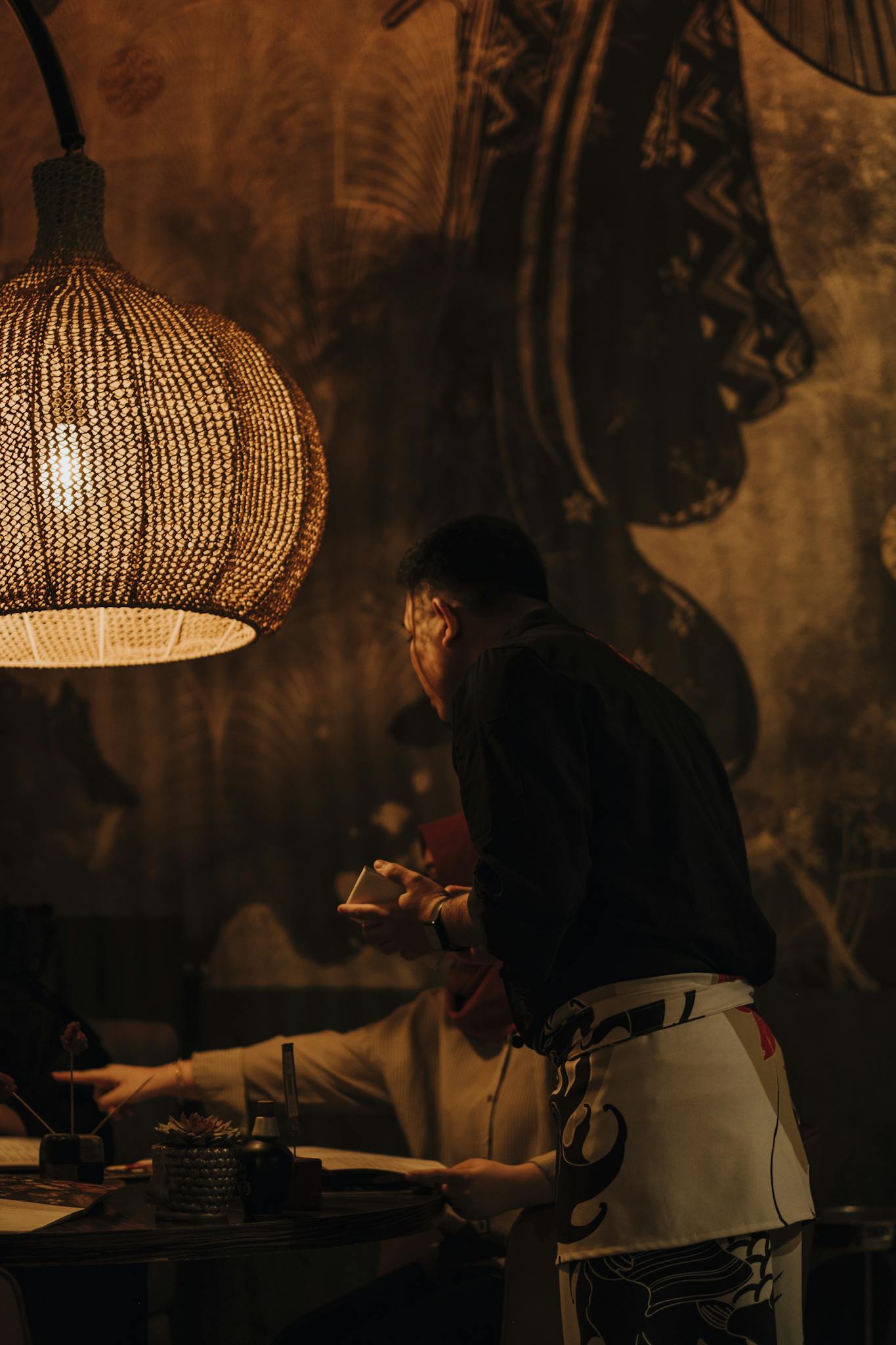 Dimly lit restaurant with waiter serving a table, emphasizing warm ambiance.